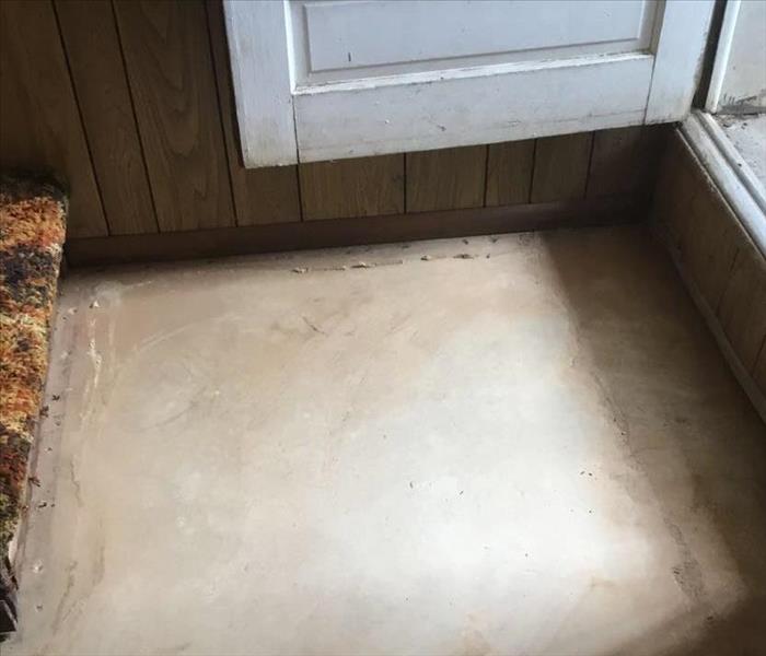 Concrete floor between an open door and a patch of multicolor carpet