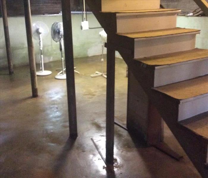 Wooden stair case in concrete basement with floor stands in the background