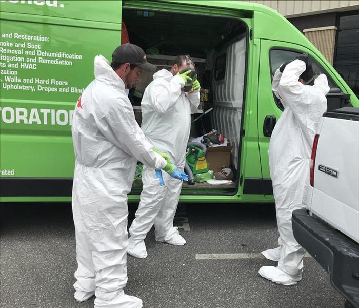 3 men put on PPE in a parking lot next to a SERVPRO vehicle