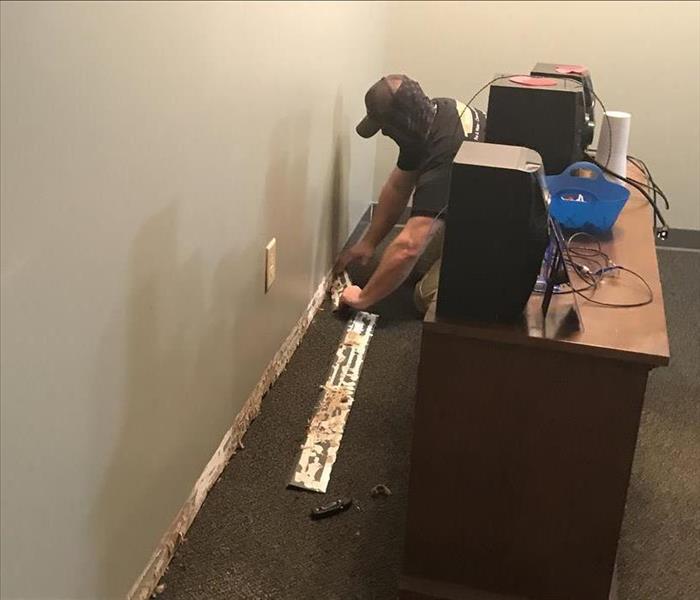 SERVPRO employee wearing face covering removes baseboard from wall