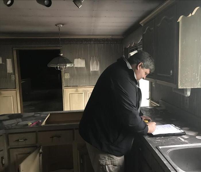 Man writing on a document in a kitchen with soot and smoke damage