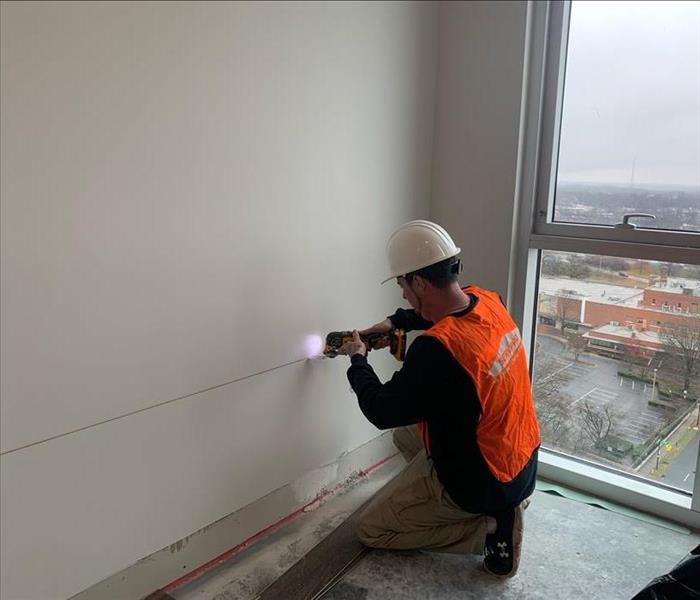 Man in orange SERVPRO safety vest cuts a line into a white wall
