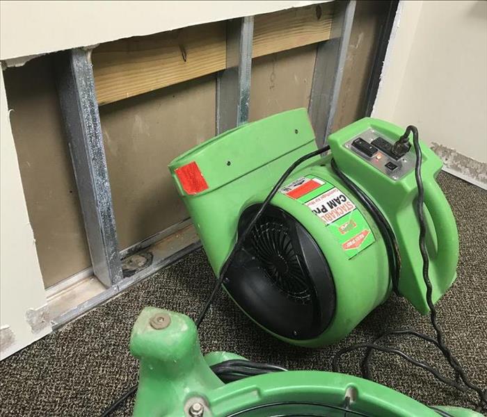 Green air mover facing wall with a section of missing drywall