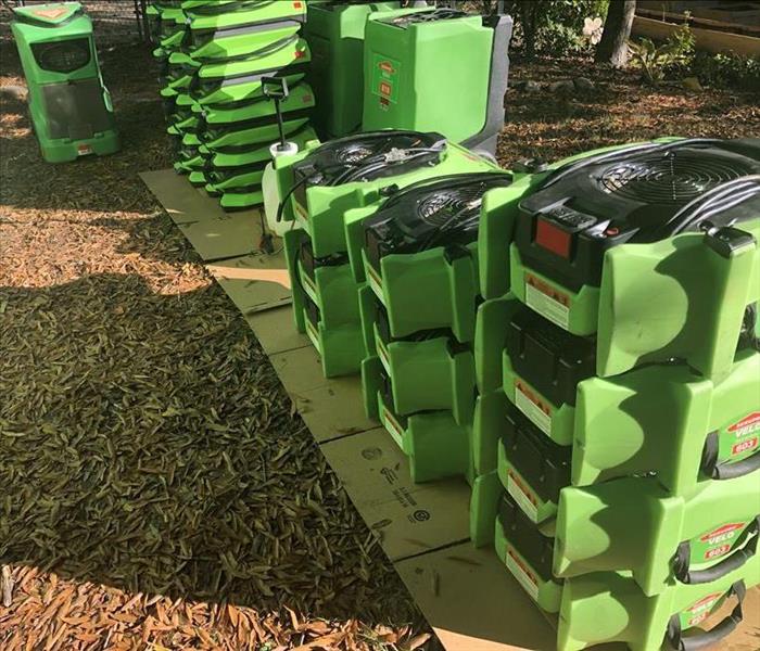 Green air movers and dehumidifiers lined up on a sidewalk