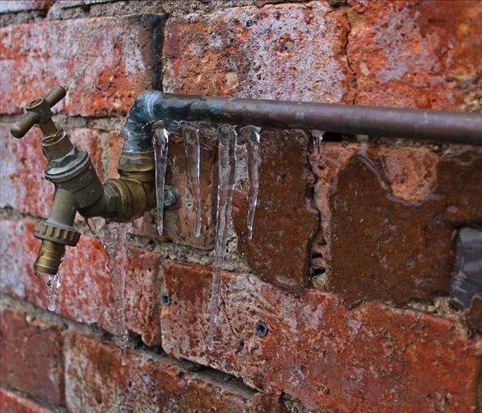 Ice covers pipe along a brick wall